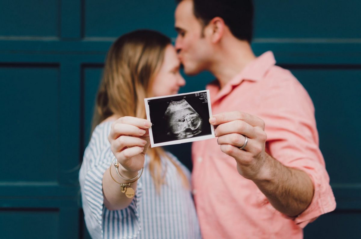 pregnant woman kissing partner holding ultrasound echo picture
